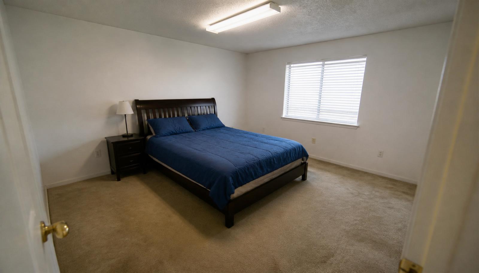 Basic bedroom with plain walls, dark wood bed and worn carpet before AI bedroom redesign