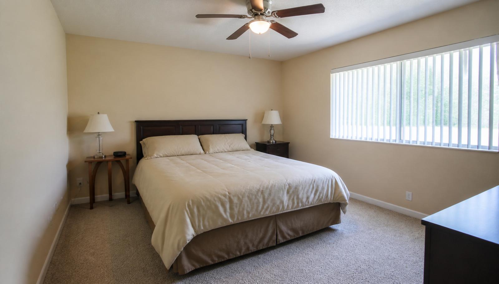 Standard bedroom with basic wood headboard, beige carpet and ceiling fan before AI bedroom redesign